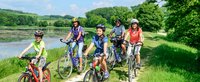 Familie fährt zusammen mit dem Rad am Wasser aus dem Wald entlang