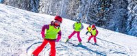 Vier Kinder auf Ski fahren eine Strecke entlang