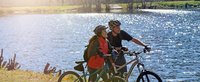 Frau und Mann stehen mit Mountainbike am Wasser und schauen in die Ferne