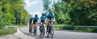 Vier Rennradfahrer fahren hintereinander an einer Straße entlang