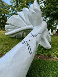 große Feder-Skulptur auf einer Wiese mit Fokus auf eine Unterschrift darauf